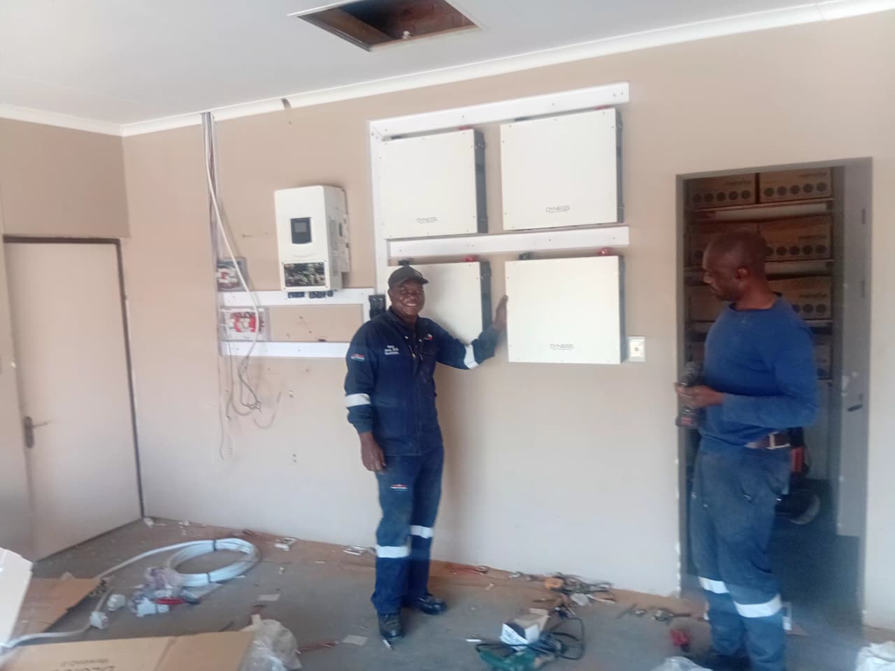 Technicians beside a wall-mounted battery storage and inverter installation